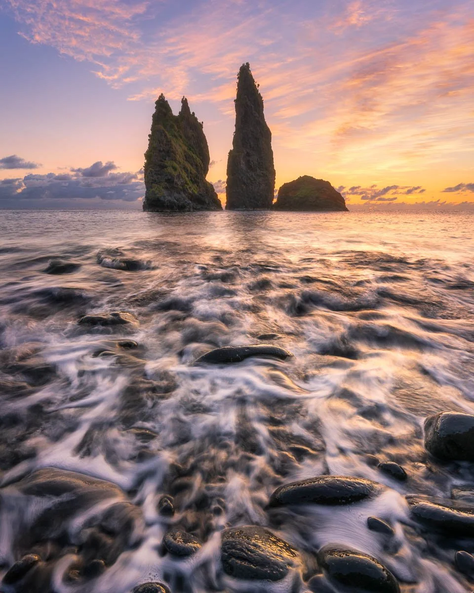 Sea stacks during sunset with rocks and waves in the foreground.