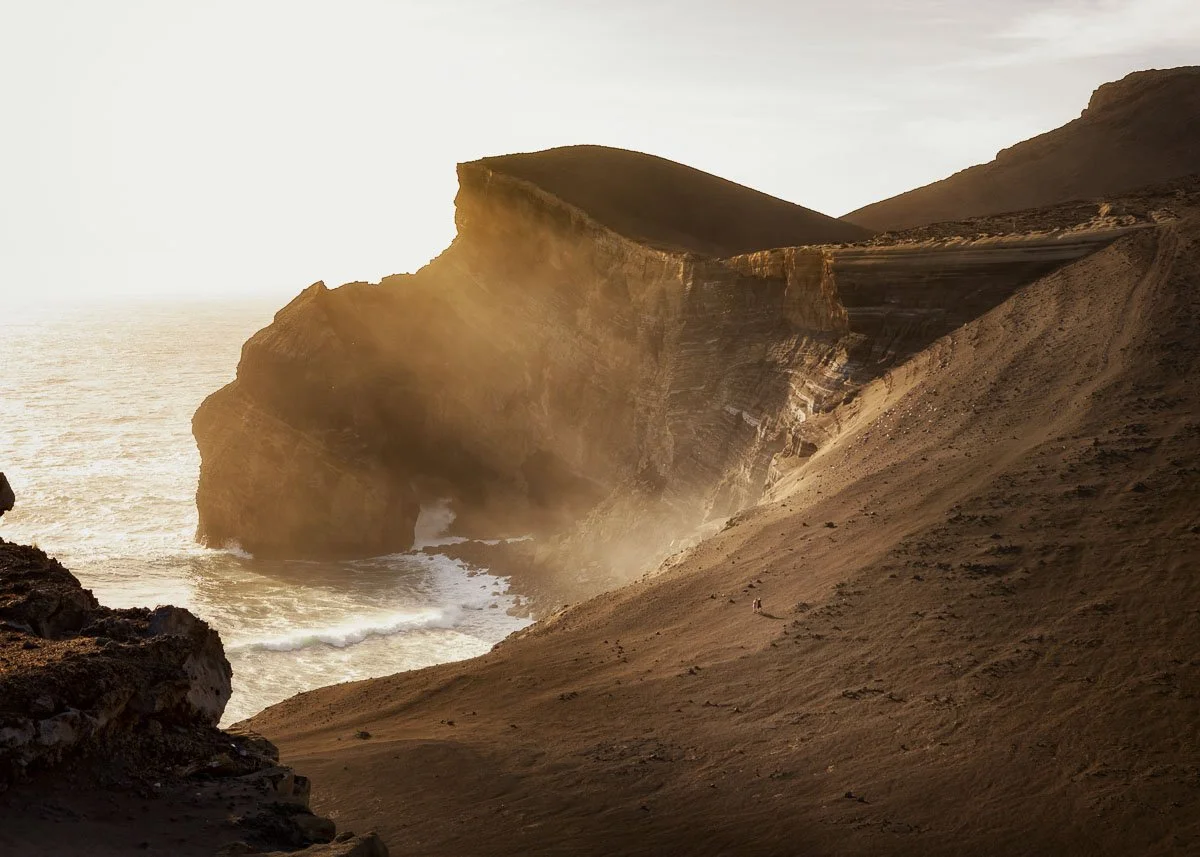 Sunset over rugged coastal cliffs with waves crashing at the base.