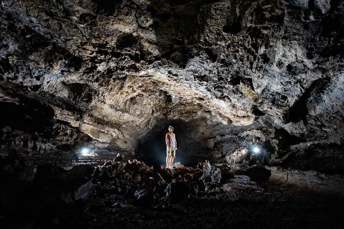 A person standing inside a dark, rocky cave illuminated by two bright lights on either side.