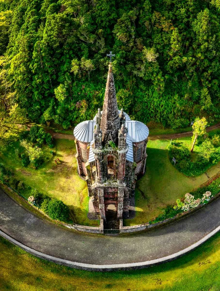 A church with a tall spire surrounded by lush green trees and grassy areas, viewed from above.