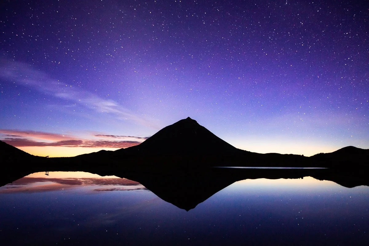 A mountain reflection in a lake at dusk under a starry sky.