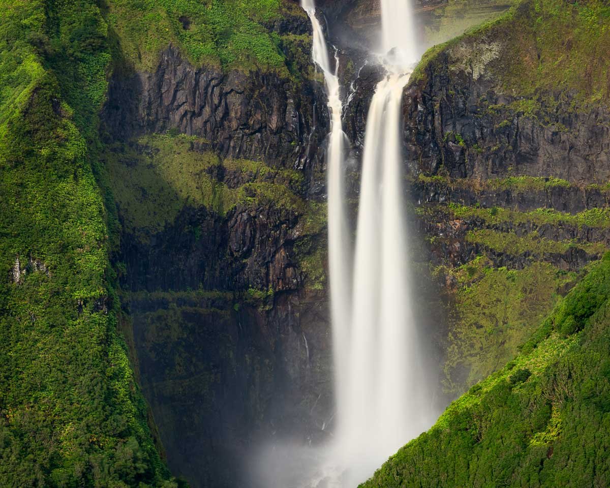 Tall waterfall cascading down a rocky cliff surrounded by lush green vegetation.