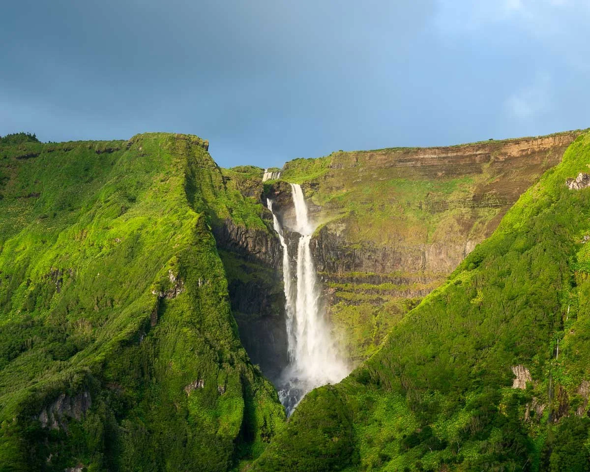 Serene waterfall cascading down lush green cliffs under a clear sky.