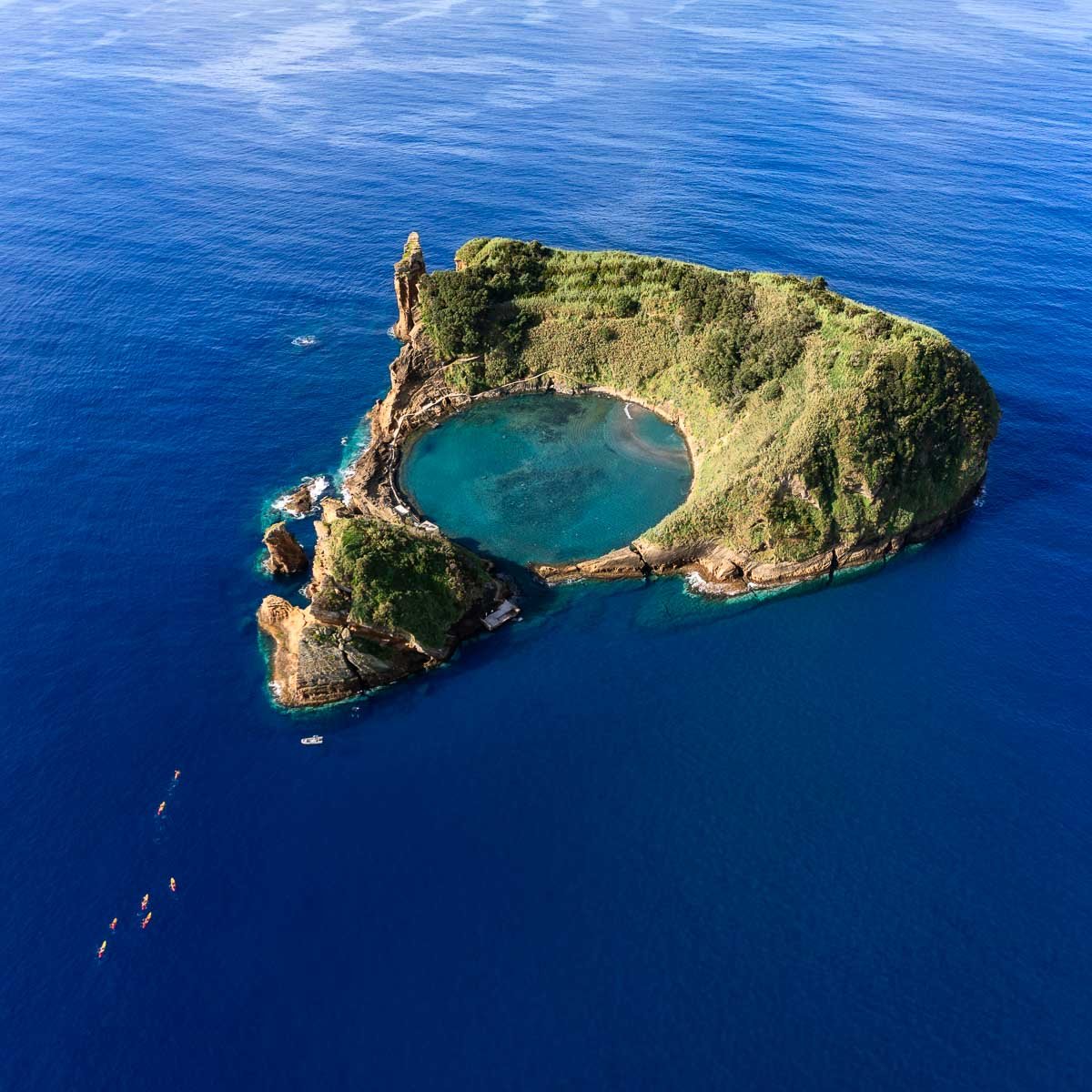 Aerial view of the iconic volcanic island, Umpaku, with a crater lake in the center, surrounded by lush green vegetation and deep blue ocean.
