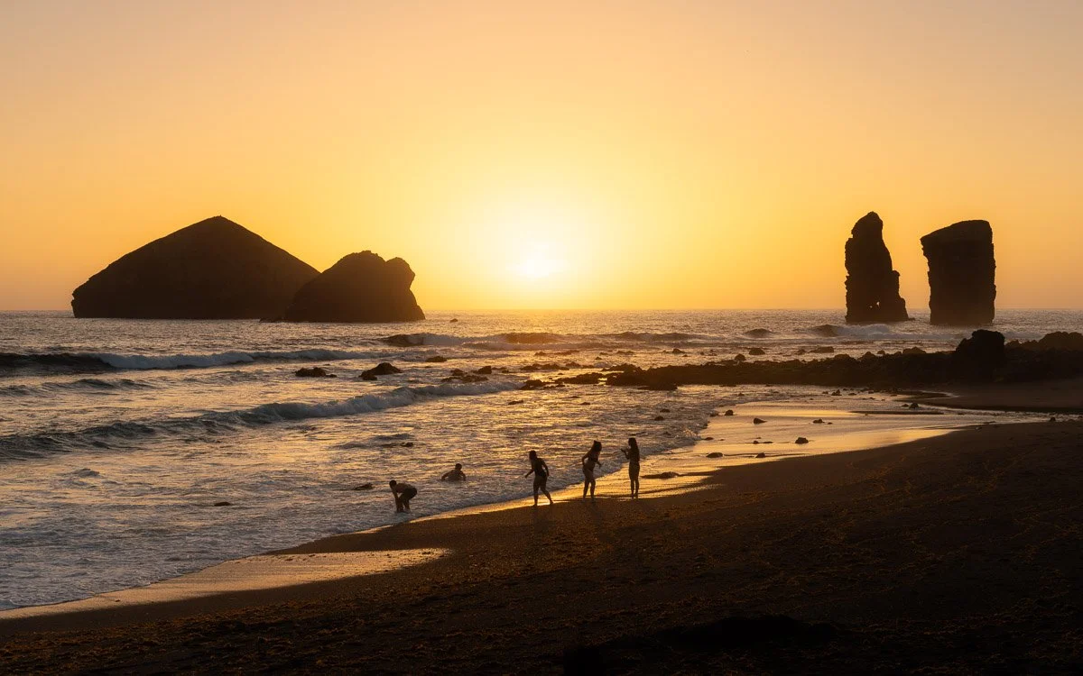 People on a beach at sunset with rock formations in the water