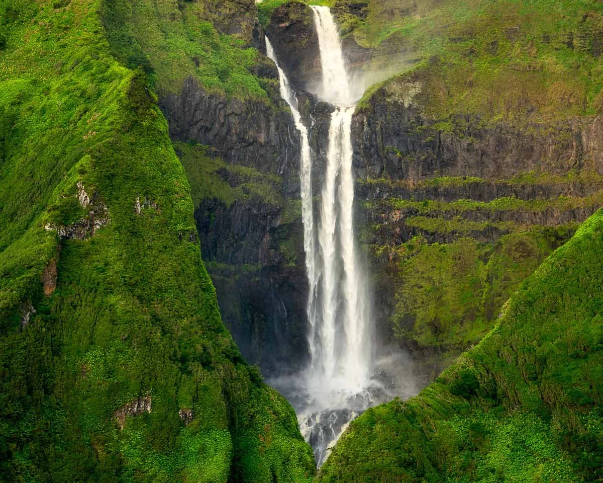 A tall, multi-tiered waterfall cascading down a green mountainside with lush vegetation.