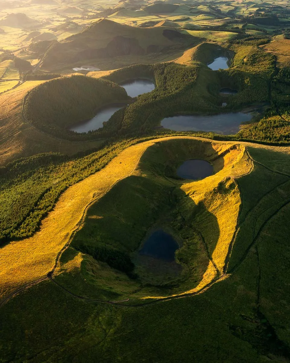 Aerial view of a landscape with multiple crater lakes surrounded by green hills and fields.