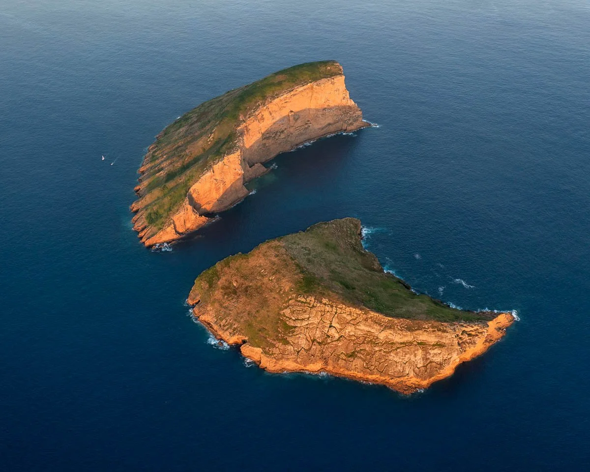 Aerial view of two large, rocky, green-covered islands surrounded by ocean water.