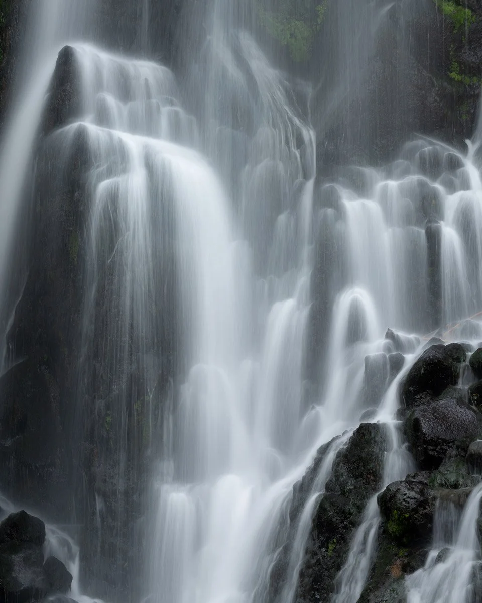 Waterfalls cascading over dark rocks in a lush green forest.
