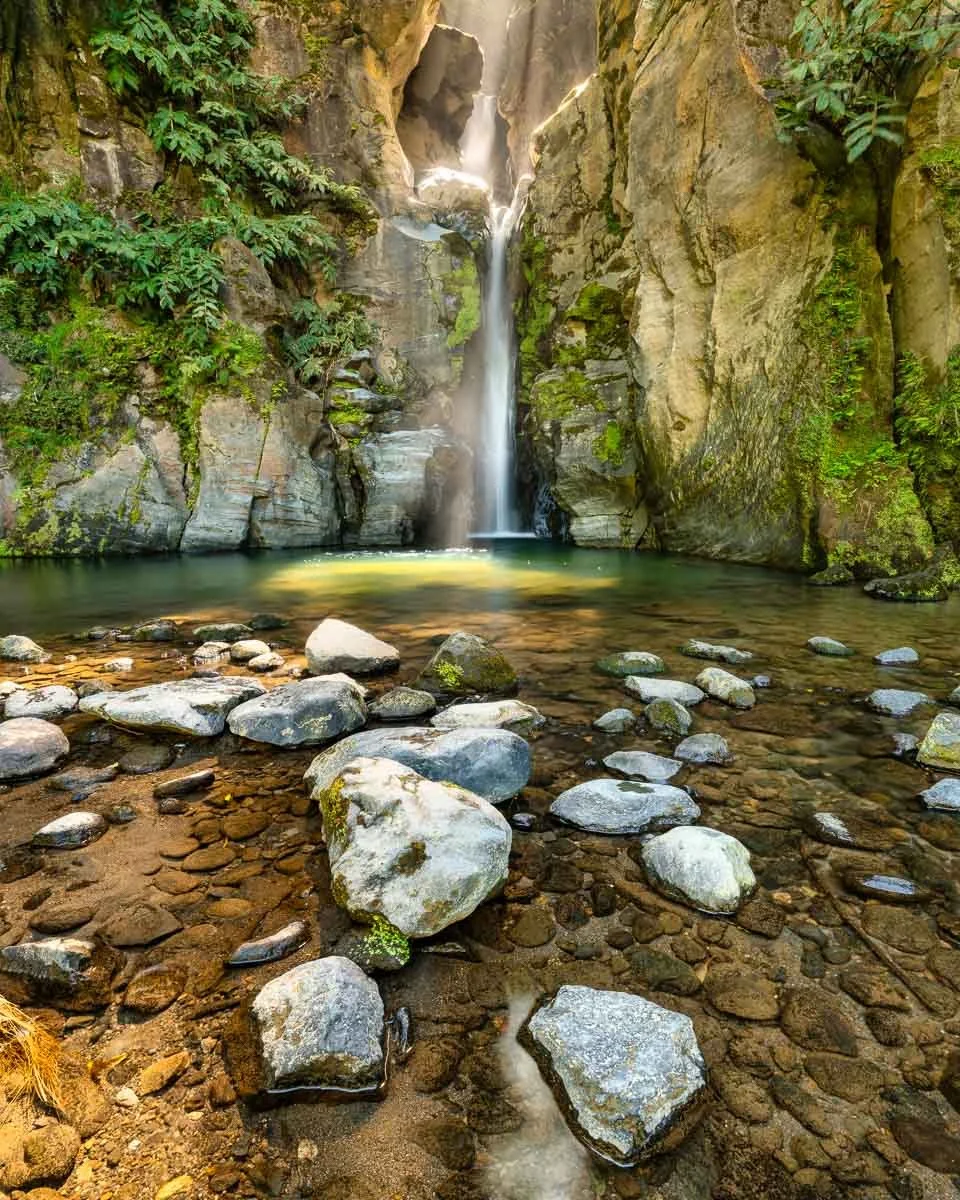 A waterfall flowing into a pool of water surrounded by rocks and lush green vegetation.