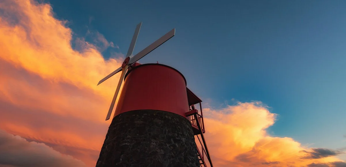 A red windmill with four blades against a colorful sunset sky with orange and blue clouds.