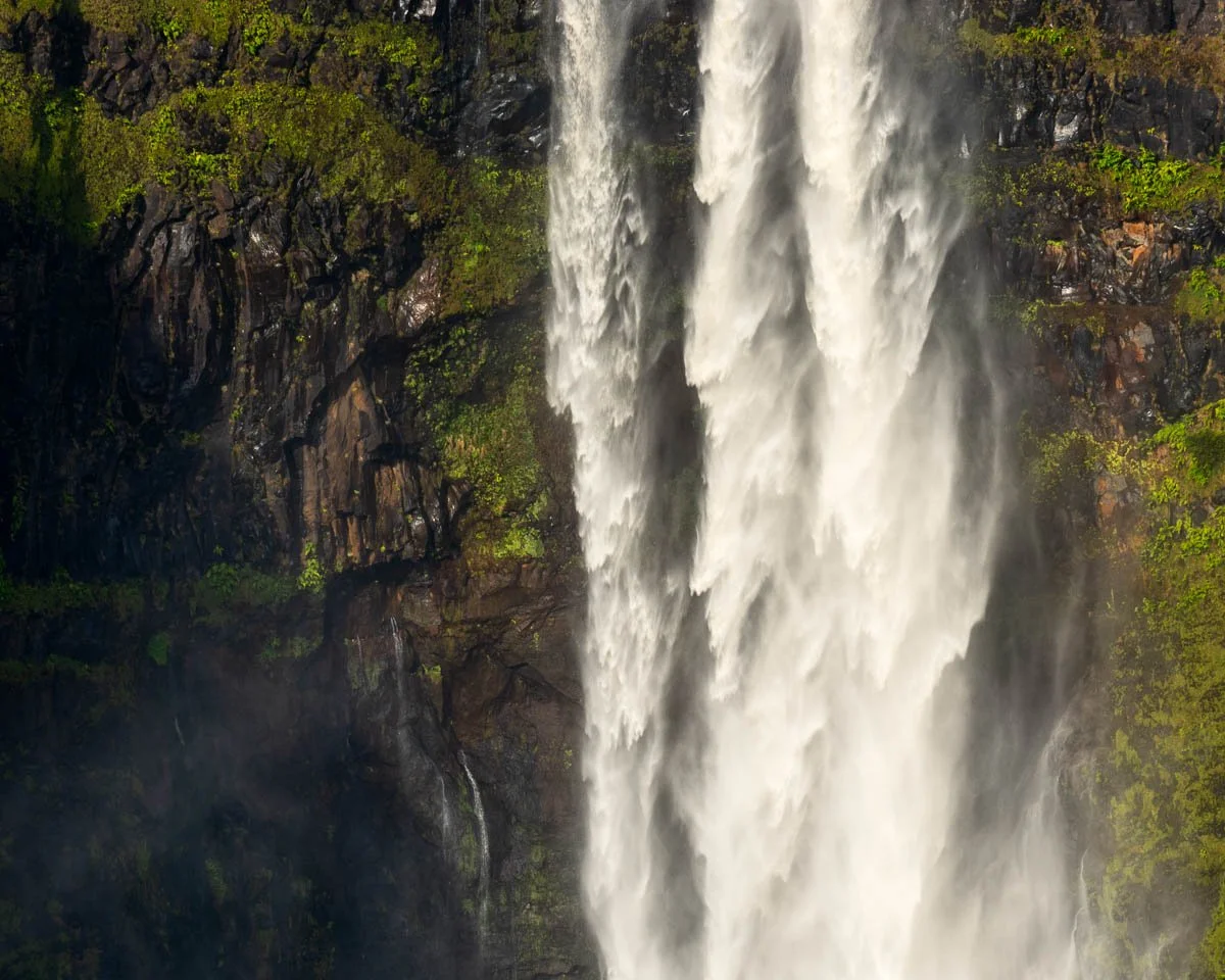 A tall waterfall cascading down a rocky cliff surrounded by lush green trees.