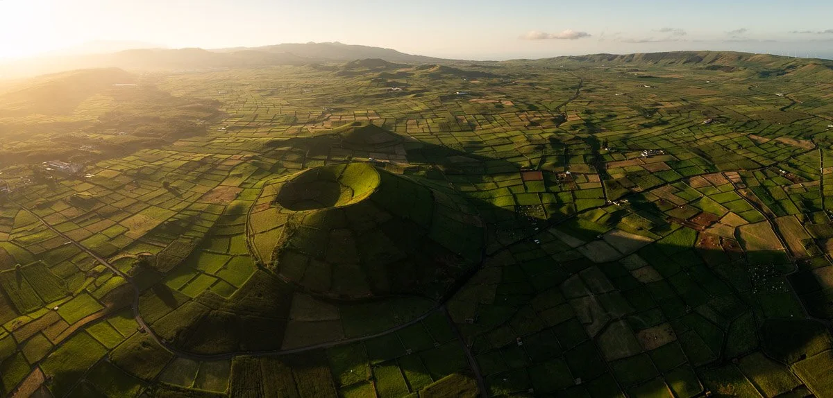 Aerial view of patchwork farmland with rolling hills and a circular hill in the center, during sunset.