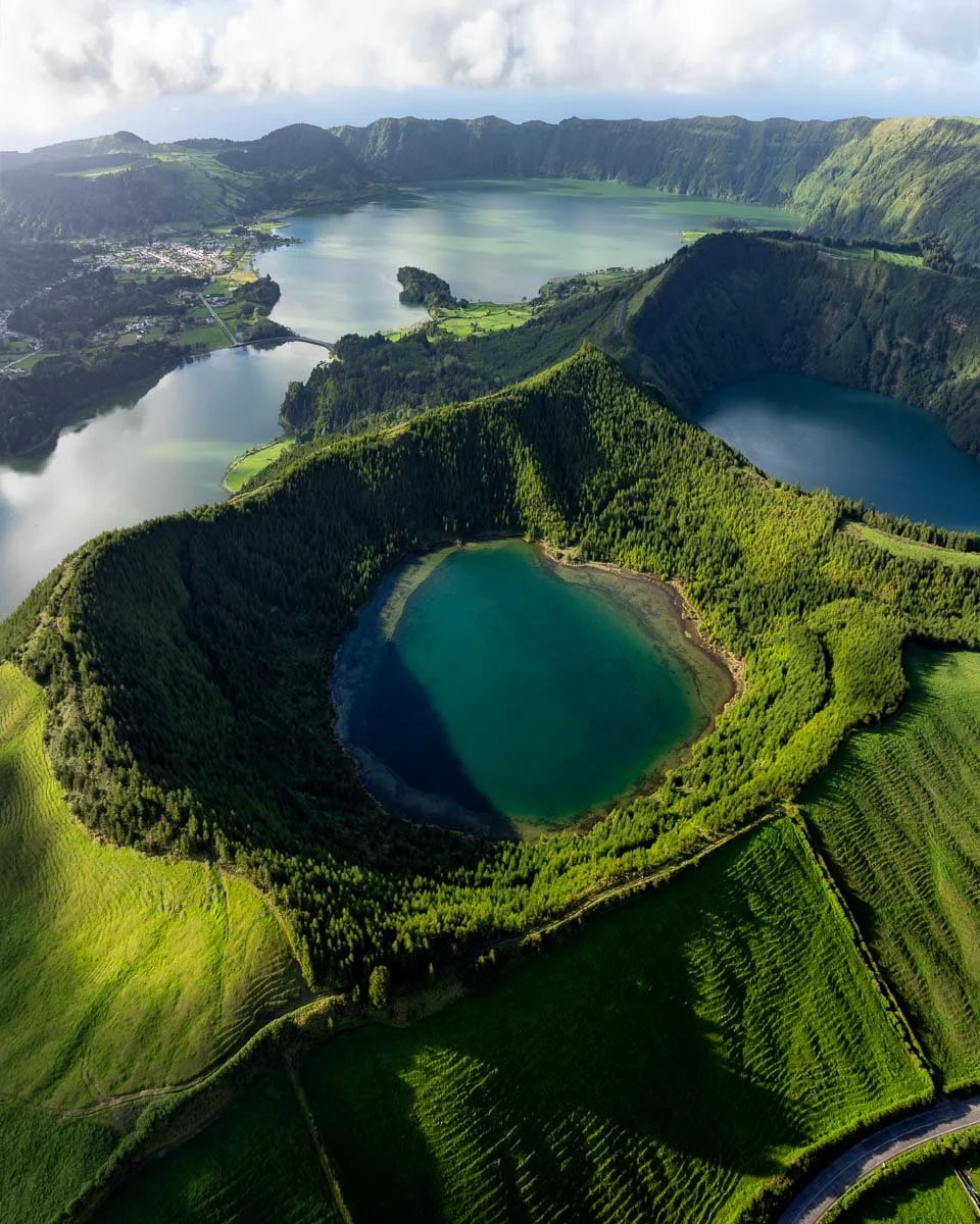 Aerial view of a volcanic crater lake surrounded by lush green forested hills and additional lakes in the background.