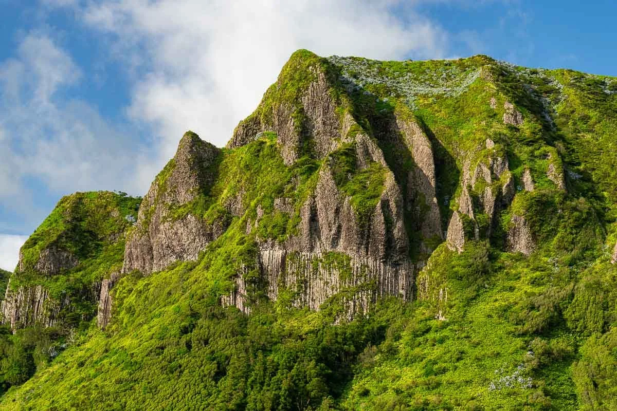 Green moss-covered rocky mountain with dramatic peaks and blue sky in the background.