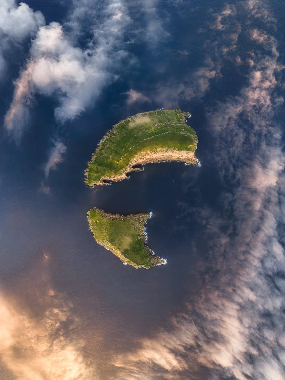 Top-down aerial drone photograph of Ilhéu das Cabras volcanic formations surrounded by low clouds on Terceira Island, Azores.