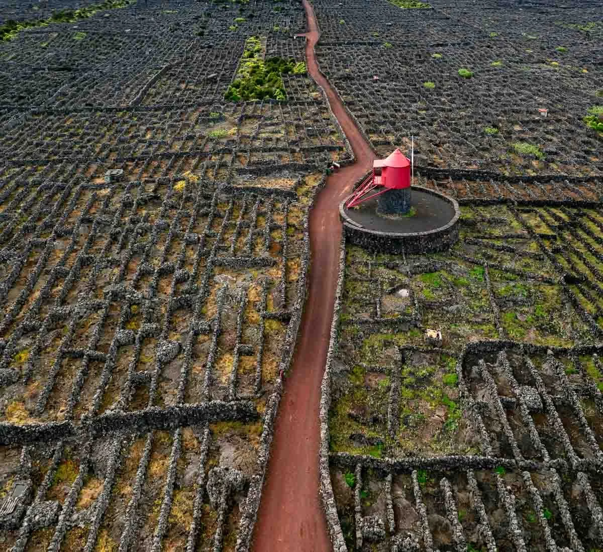 An aerial view of a rock landscape with a dirt path winding through it, featuring a red and black round structure.