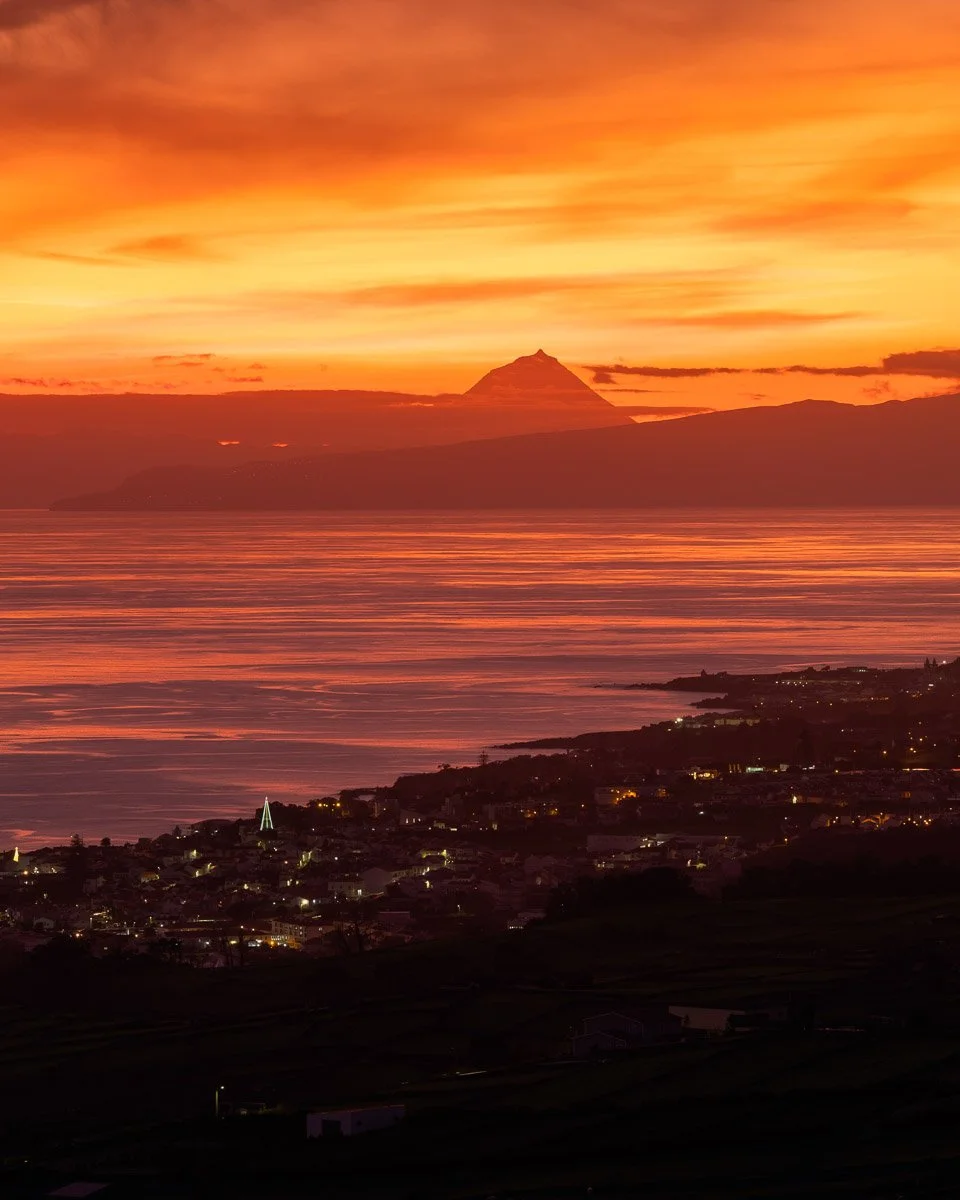 A sunset over a body of water with a mountain in the background and a town in the foreground.