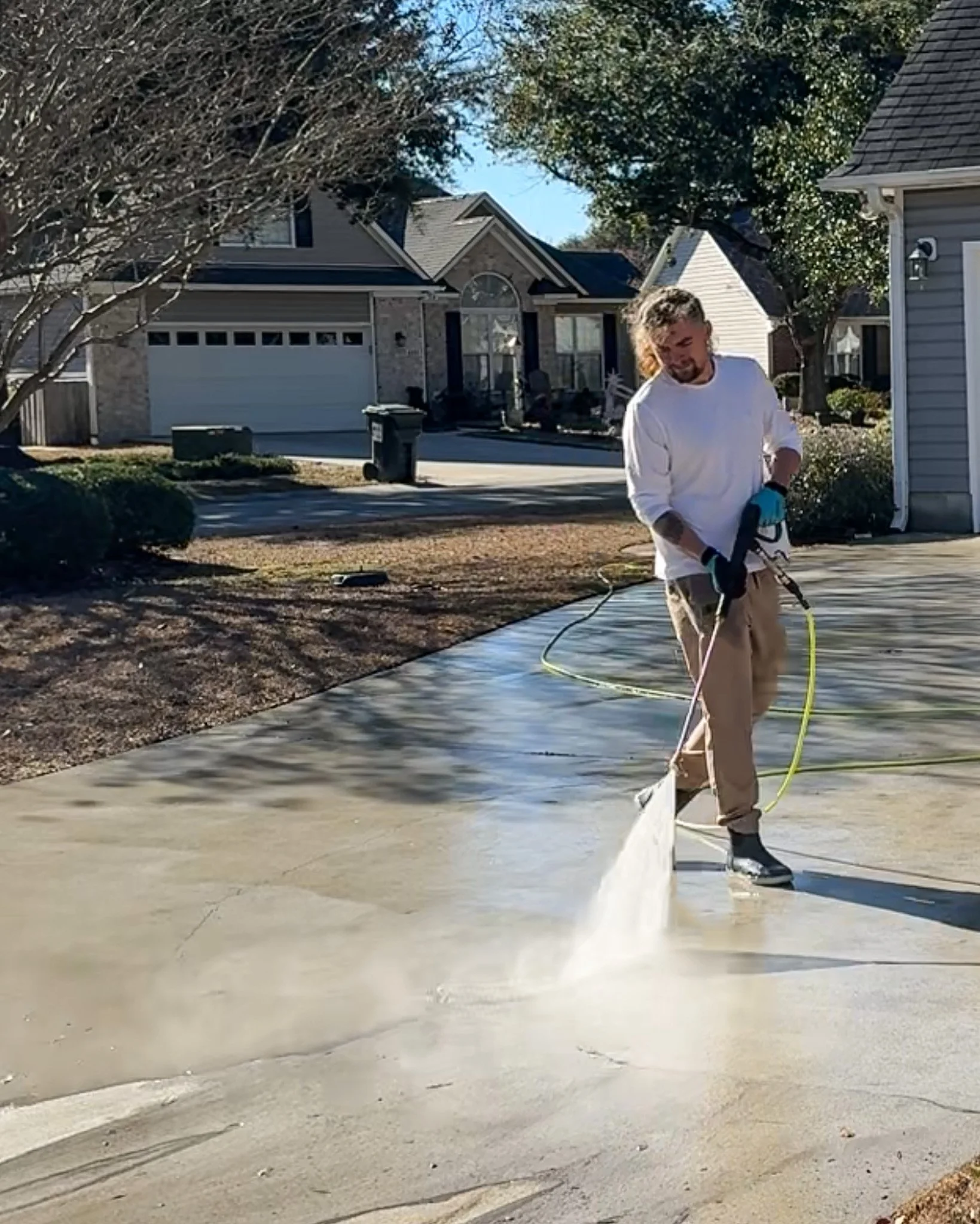 A man cleaning a concrete driveway with a pressure washer in a residential neighborhood.