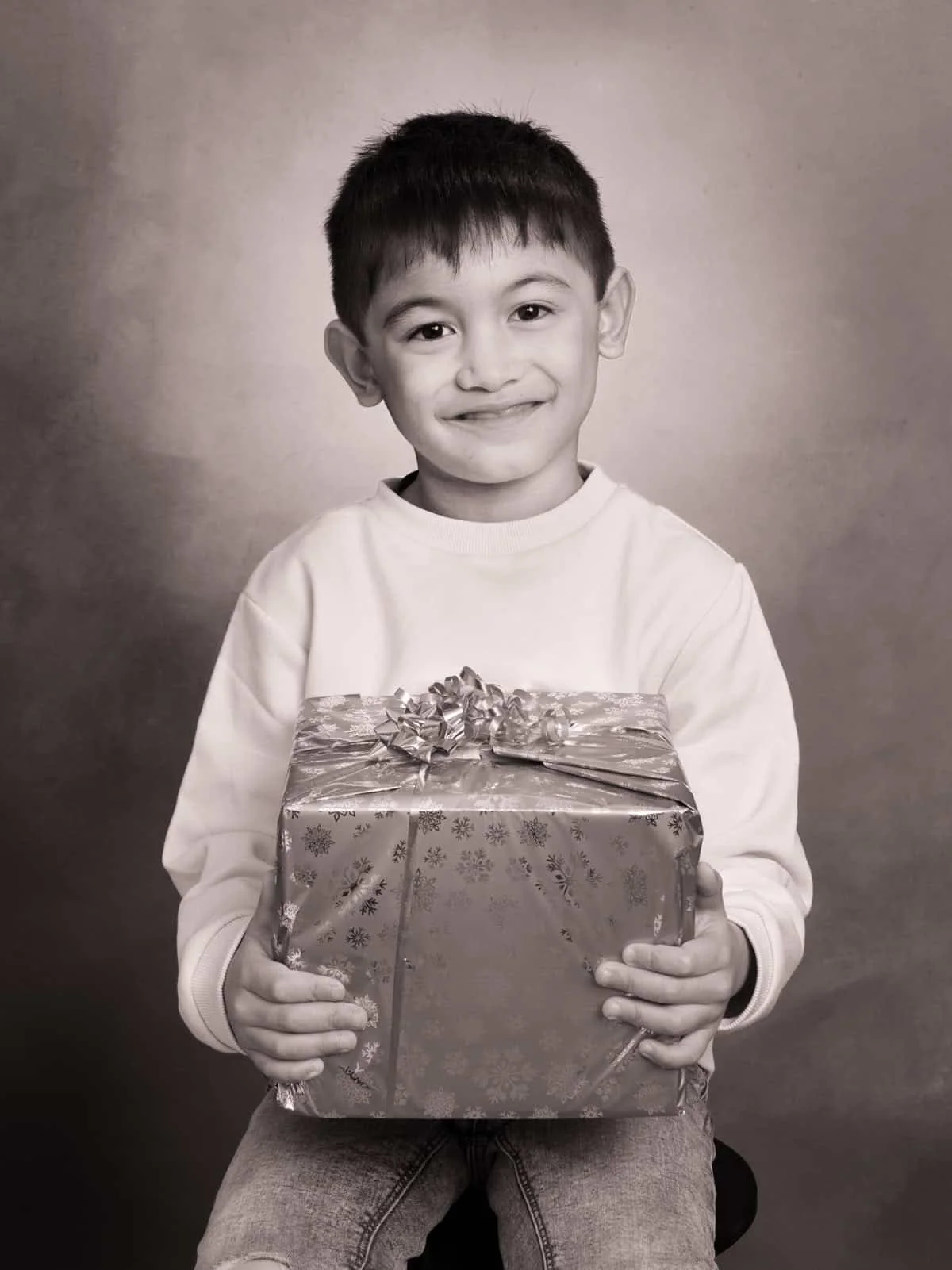 Portrait noir et blanc d’un enfant en studio à Strasbourg, souriant et tenant un cadeau.