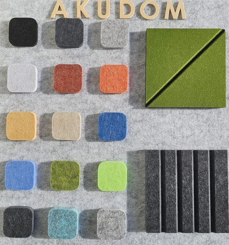 Uzornici boja i tekstura dekorativnih akustičnih filc panela, raspoređeni na sivoj pozadini, sa drvenim slovima „AKUDOM“ na vrhu. Prikaz materijala za savremene kancelarije i komercijalne prostore.