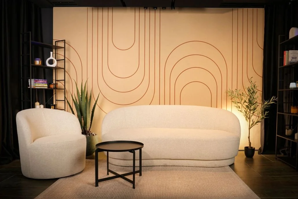 Enterijer dnevne sobe sa toplim ambijentom, tamnim drvenim podom i zidom obloženim akustičnim panelima od PET filca. Bela sofa, bež tepih i dekorativni detalji stvaraju miran i lepo uređen prostor.