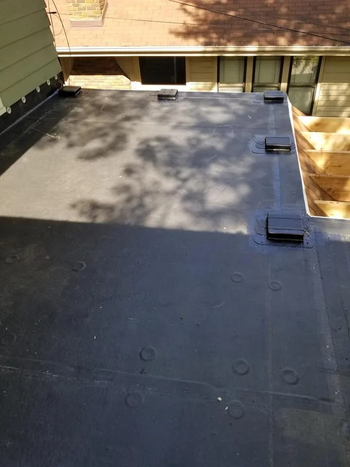 Roof with black waterproof membrane, some protruding vents or covers, and a section of unfinished wooden framing on the right side.