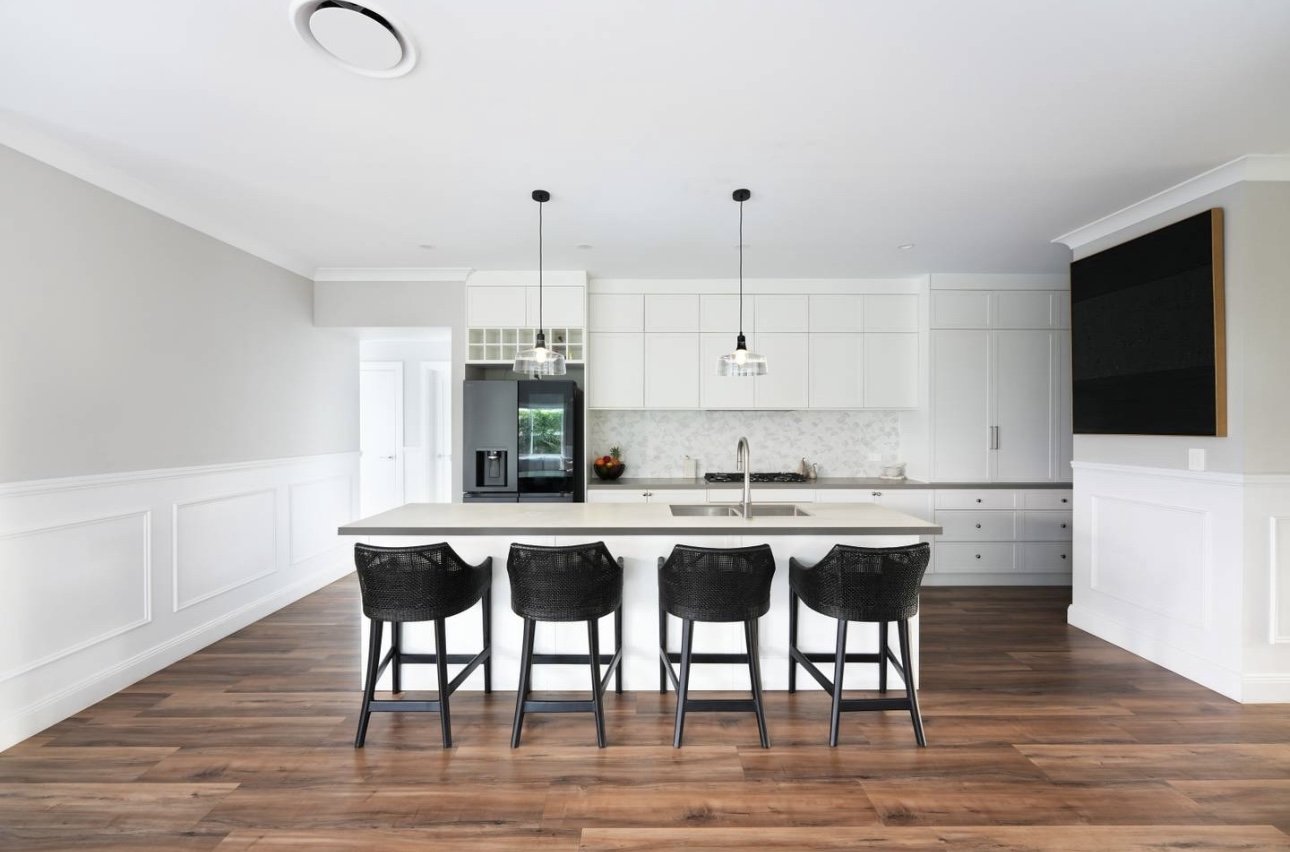 Modern kitchen with a large island, four black chairs, white cabinets, stainless steel refrigerator, and hardwood floors.