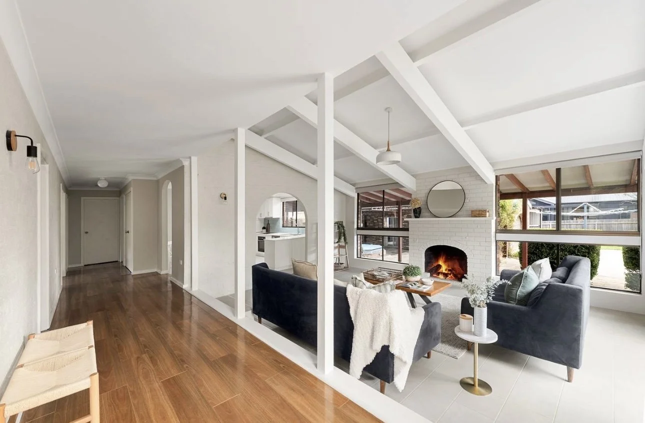 Living room with a fireplace, large windows, and modern furniture, including gray sofas, a wooden coffee table, and a side table with flowers.