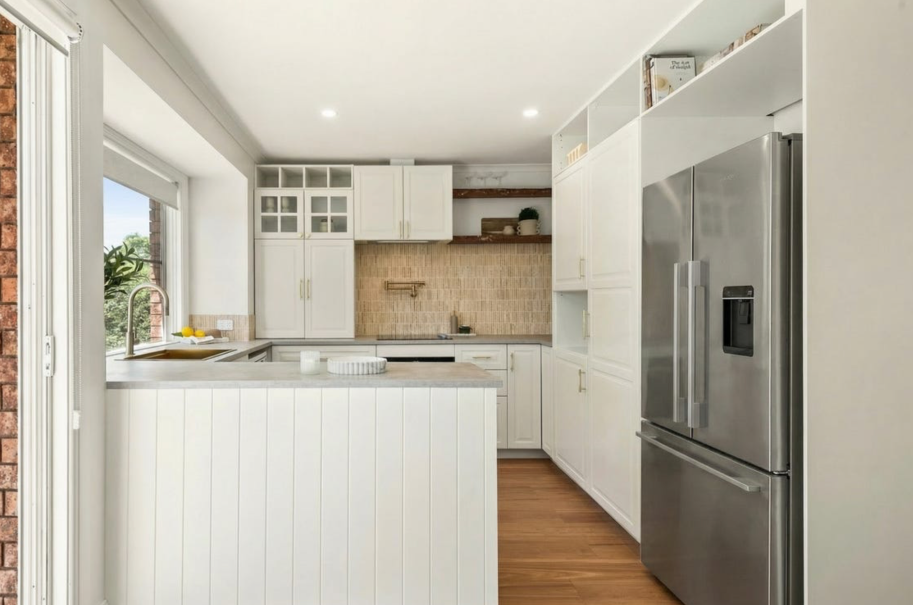 Modern kitchen with white cabinets, a stainless steel refrigerator, and a window above the sink showing outdoor greenery.