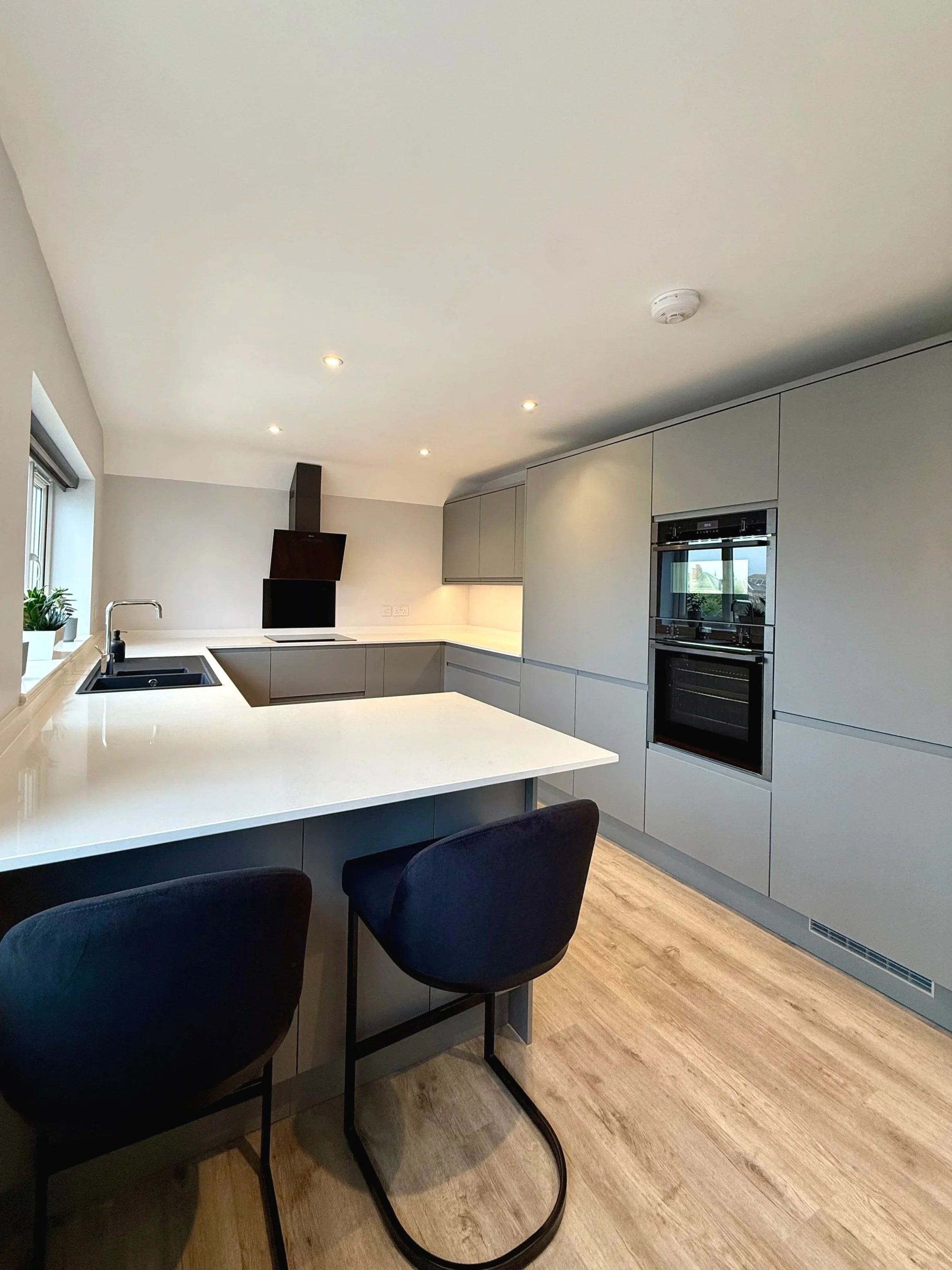 Grey j pull cabinets with oak wood flooring and white quartz worktops