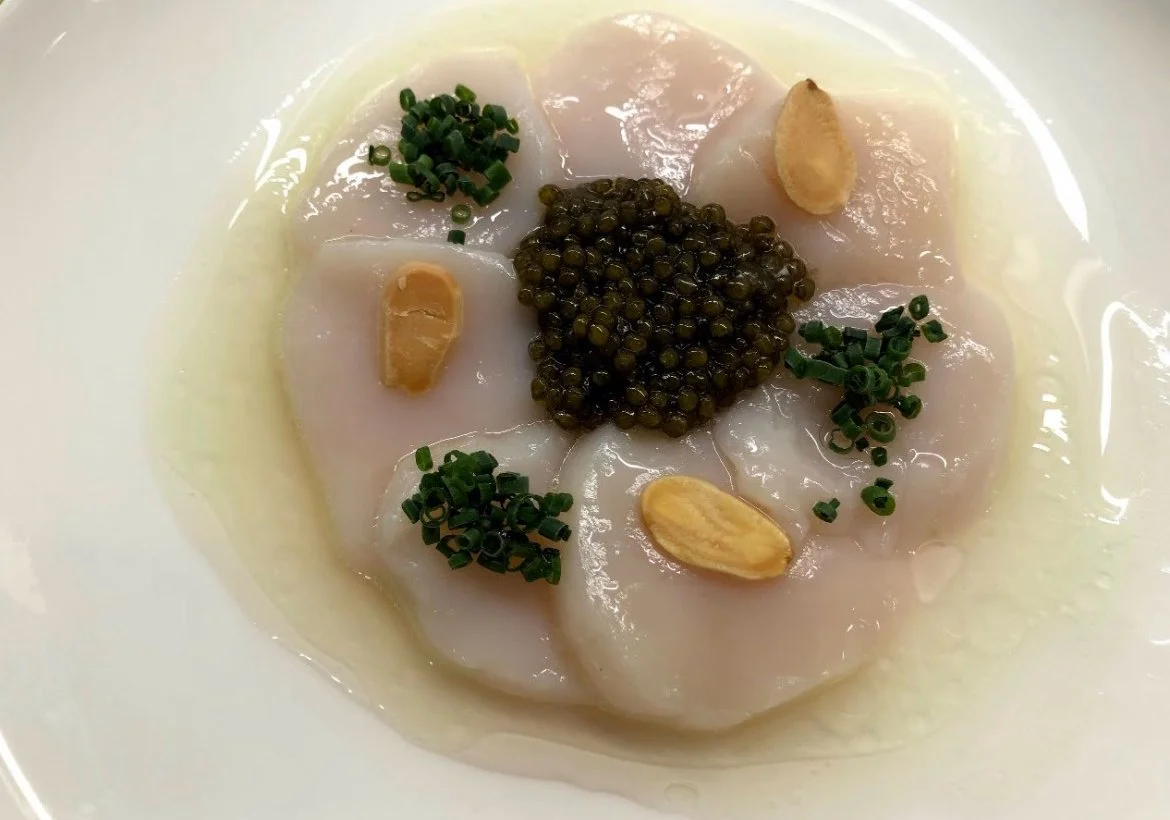 Sashimi with chopped chives, garlic, capers, and oil in a white bowl.