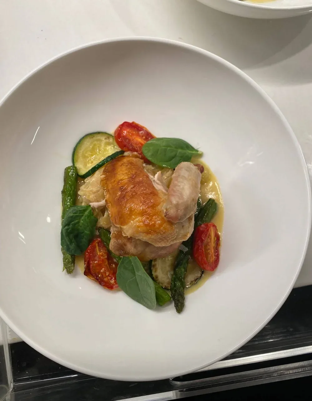 White bowl with cooked chicken, cherry tomatoes, zucchini, green beans, spinach, and yellow sauce.