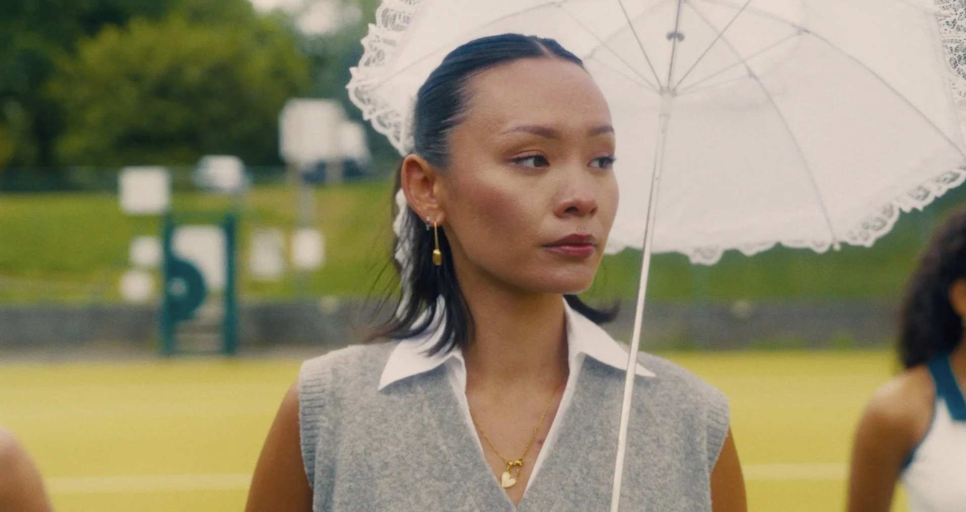 A woman in athletic clothes holding a white lace umbrella stands outdoors on a cloudy day.