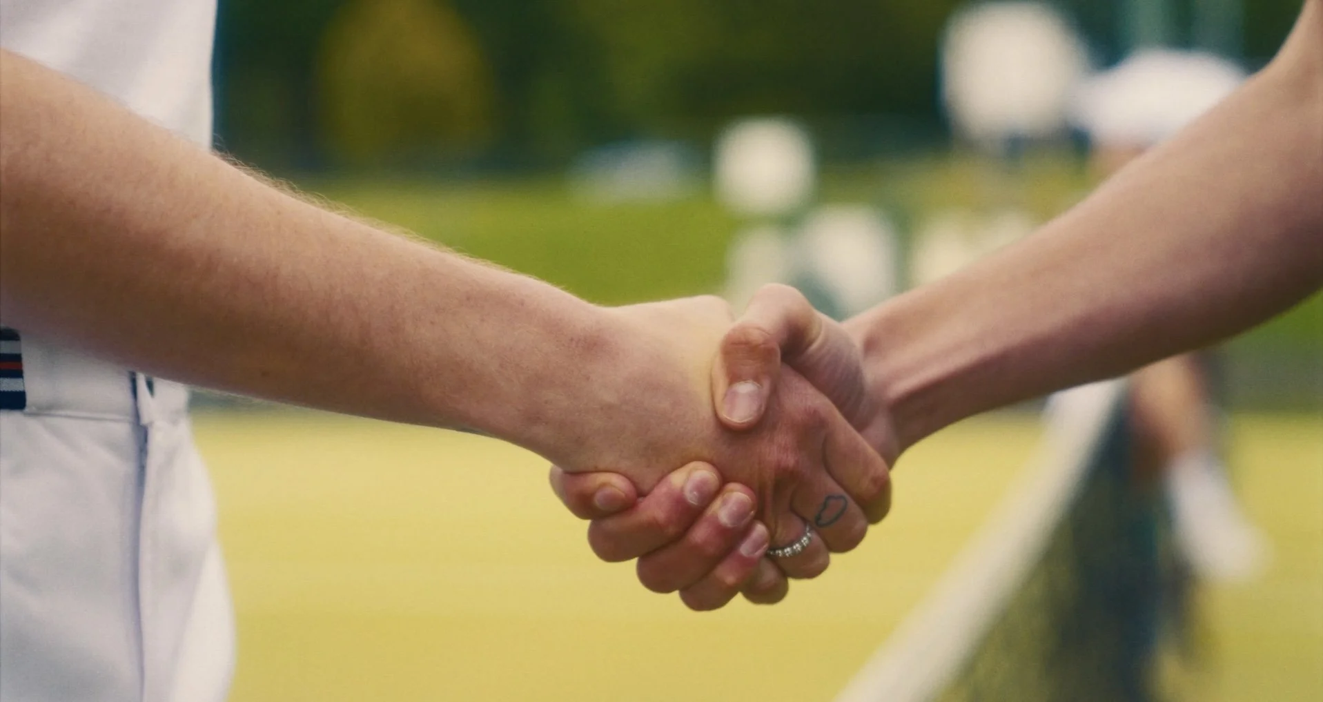 Two people shaking hands on a green field, with a blurred background.