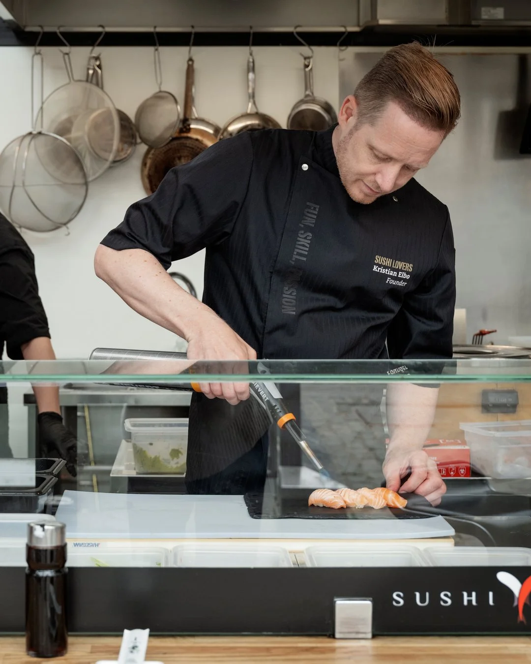 A chef slicing salmon in a sushi restaurant kitchen.