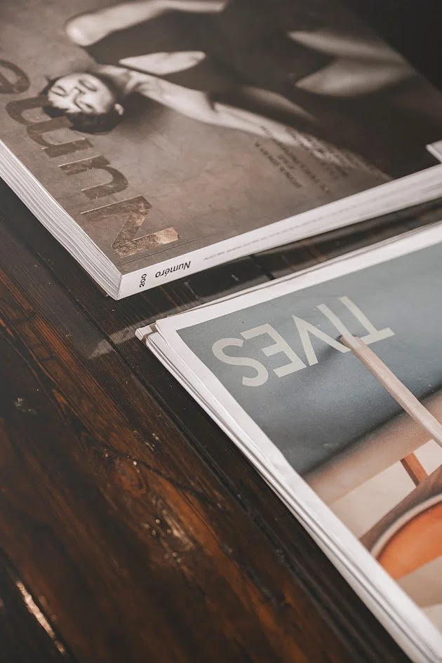 Close-up of two magazines on a dark wooden table, one featuring a woman on the cover and the other with the word 'FIVE' visible.