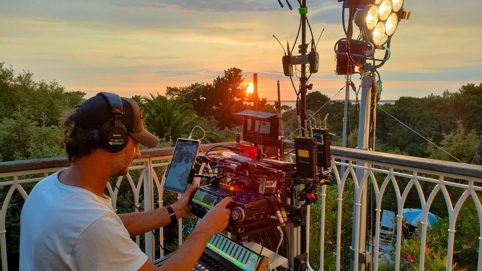 Un homme avec un casque d'écoute travaillant avec du matériel audiovisuel lors d'un coucher de soleil dans un environnement naturel.