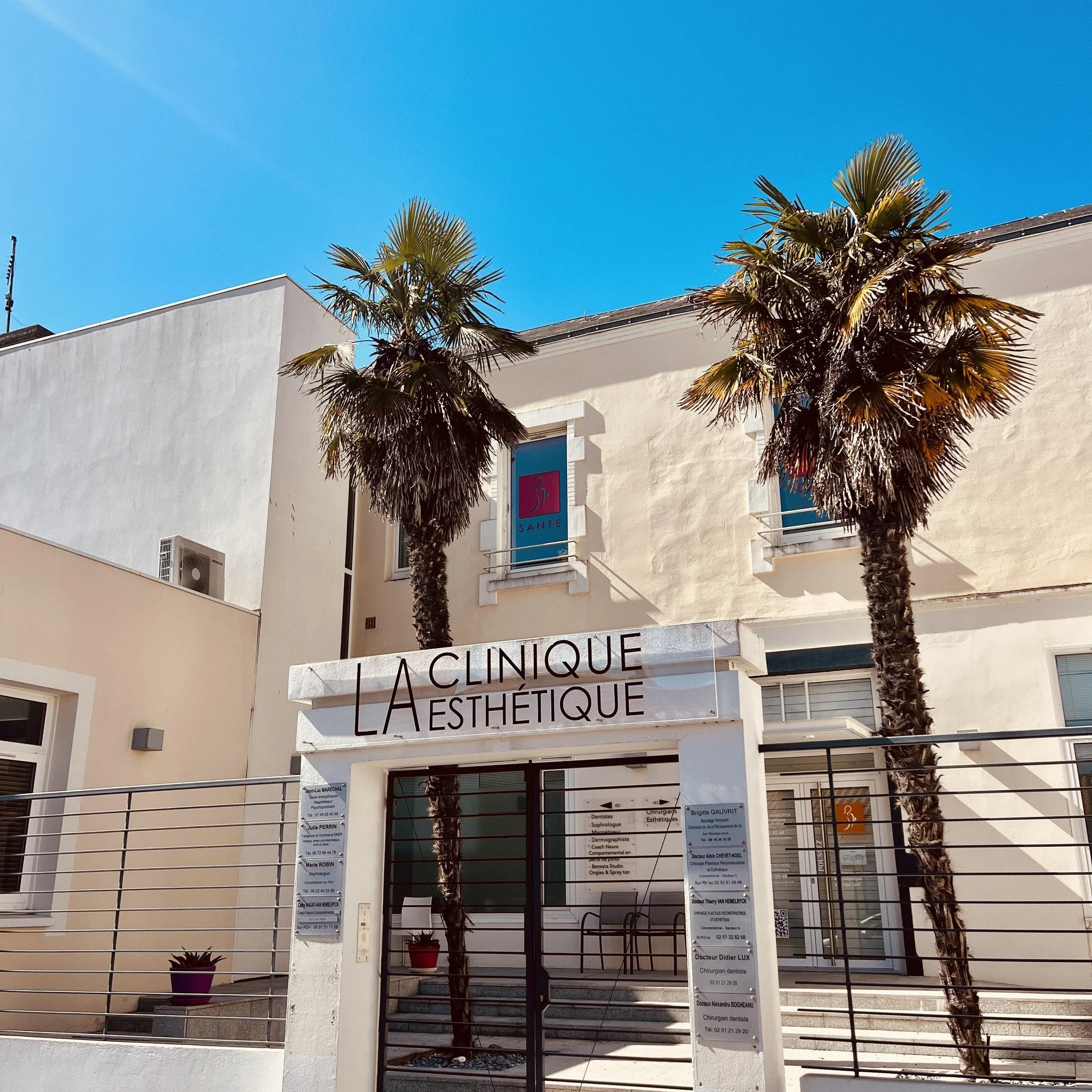 Facade de la clinique esthétique avec deux palmiers devant, sous un ciel bleu.