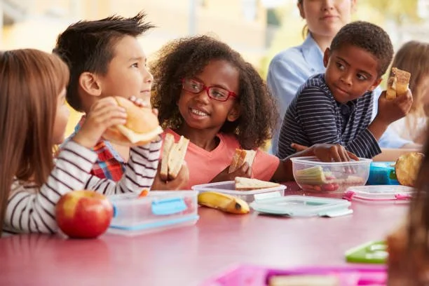 Children sitting together eating lunches at a table.