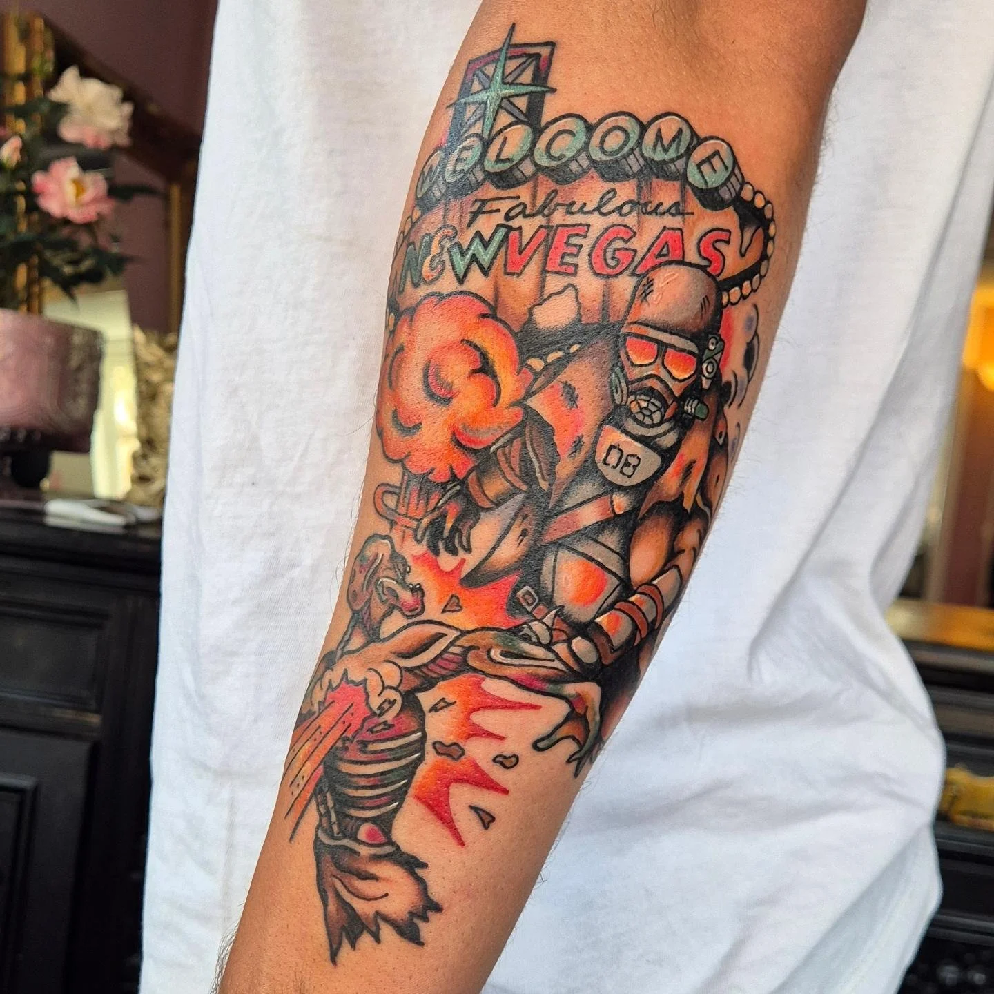 A tattoo featuring a scene insipired by the video game Fallout New Vegas. An NCR Ranger in the NCR armor is shooting a feral ghoul in front of the New Vegas sign, as a nuclear blast is going off behind them. Orange, red, and brown are the main colors