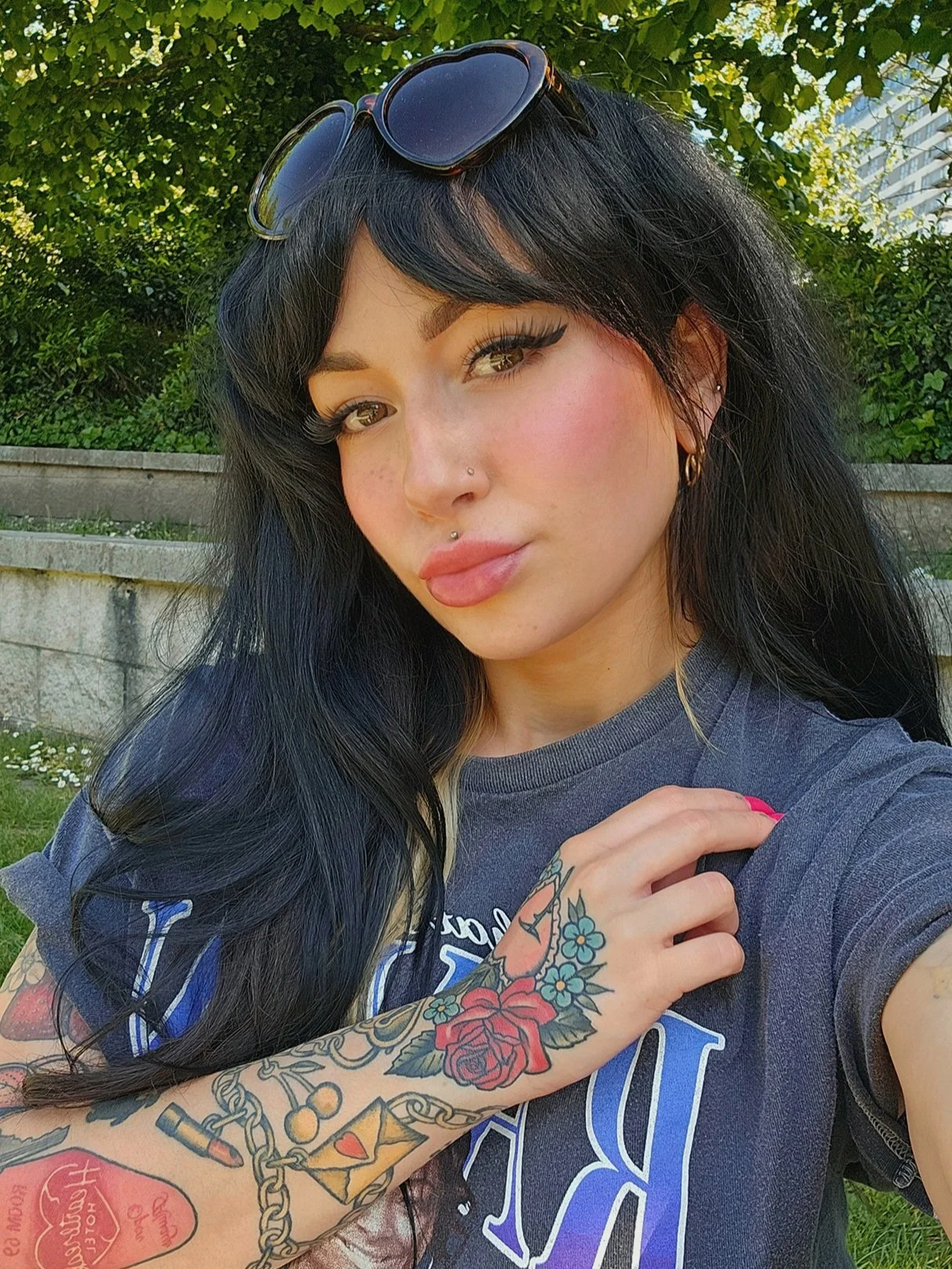 A selfie of Rachel Marion. She is white, with brown eyes and long black hair. She is wearing a grey t-shirt. Her left hand is visible, it has flower tattoos and bright pink nails.