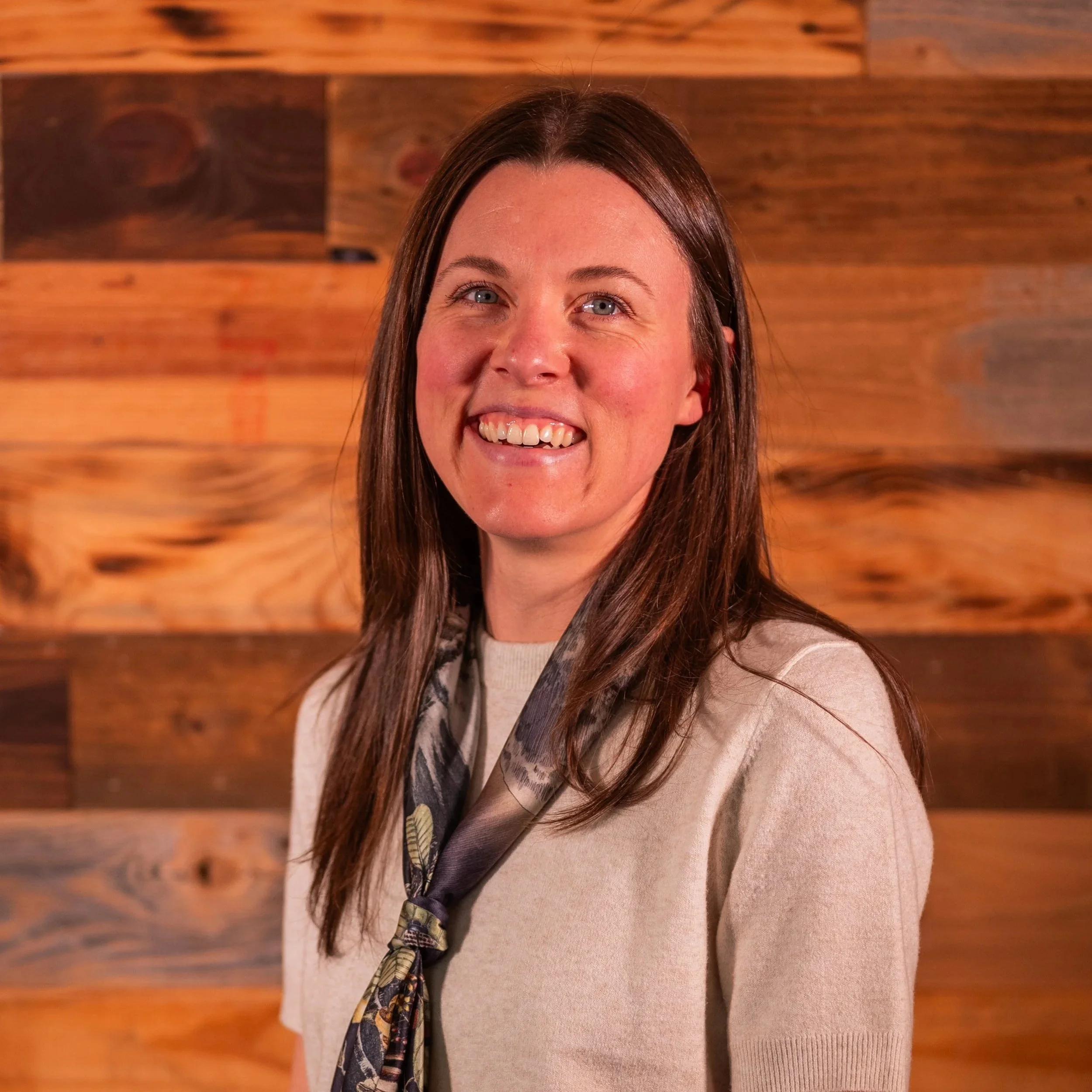 Smiling woman with brown hair wearing a red scarf and white shirt.