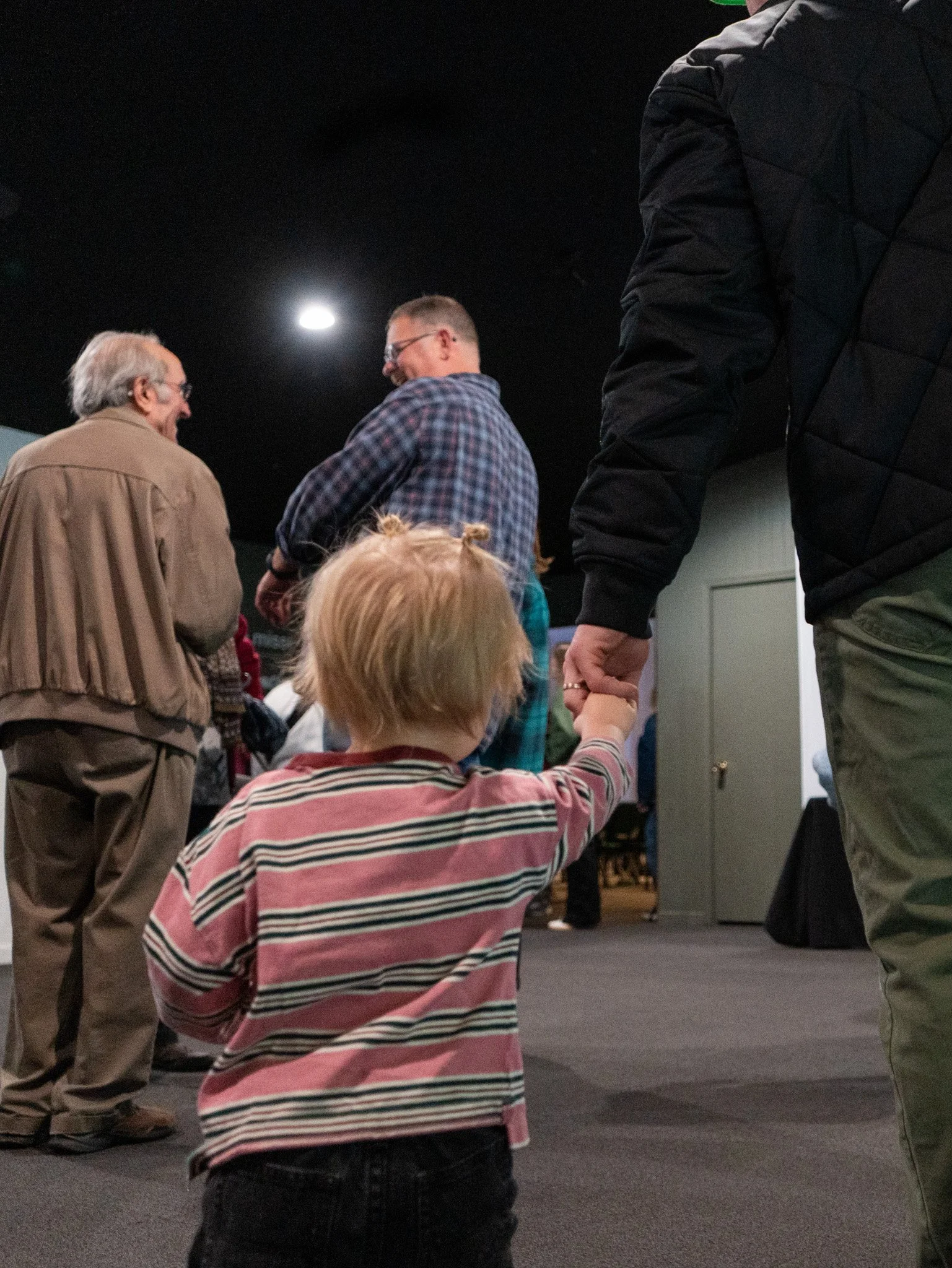 Children sitting at a table engaging in arts and crafts, one holding a paper crown, in a classroom setting.