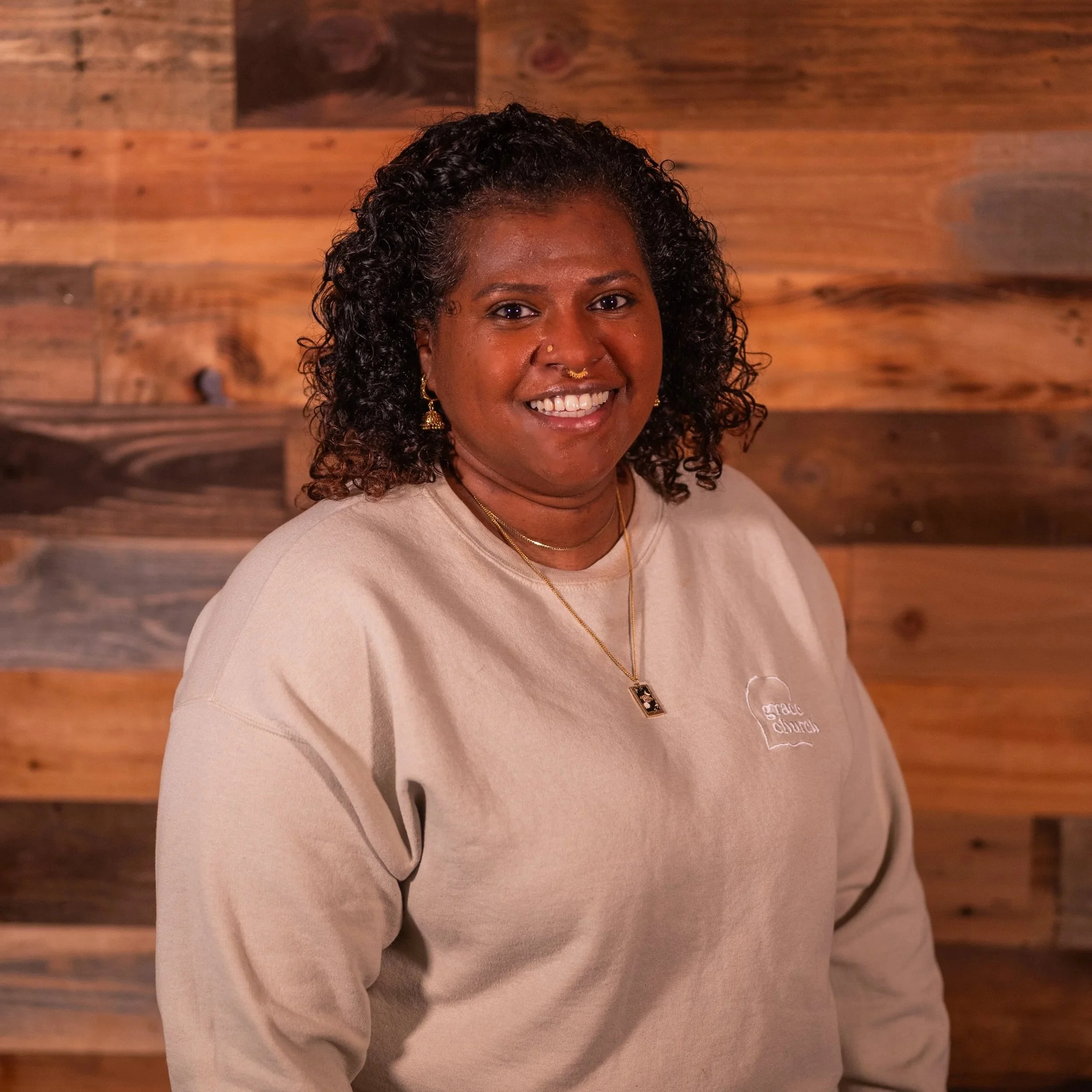 Smiling woman wearing a floral blouse and gold jewelry.