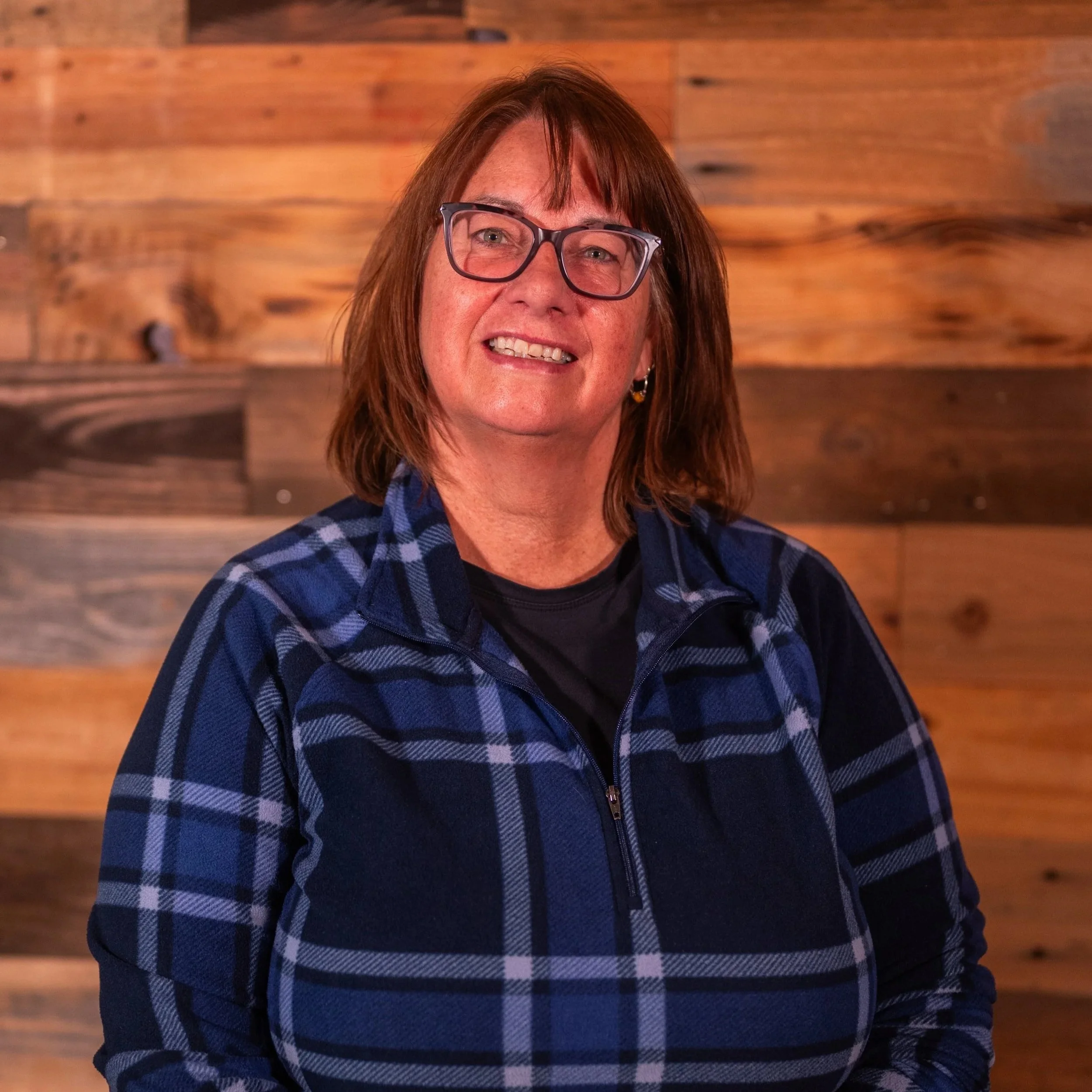 Woman with glasses smiling, wearing a blue floral pattern shirt against a light background.