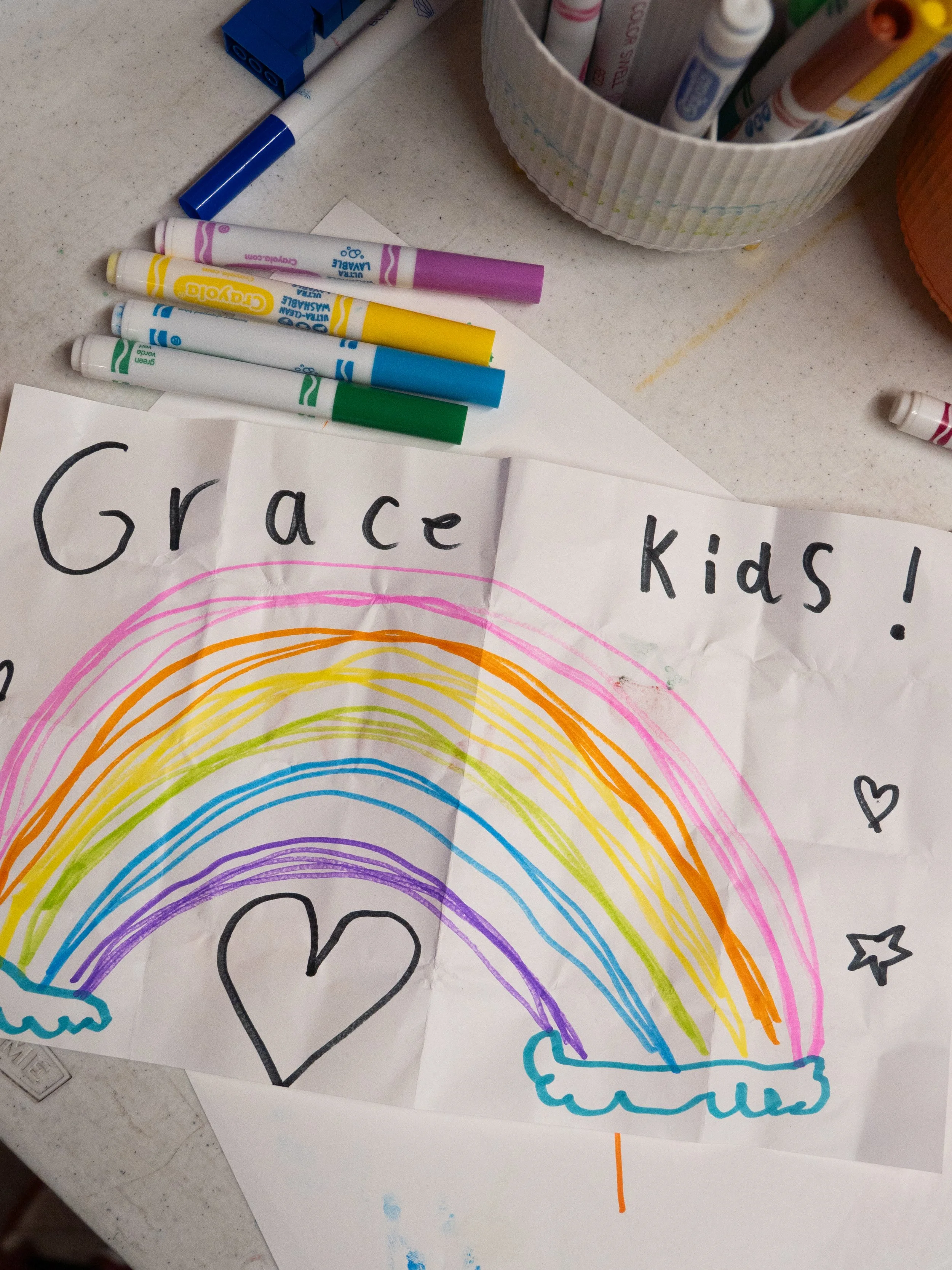 A young child and an adult indoors, the adult holding a sticker with an expression of excitement and the child smiling.