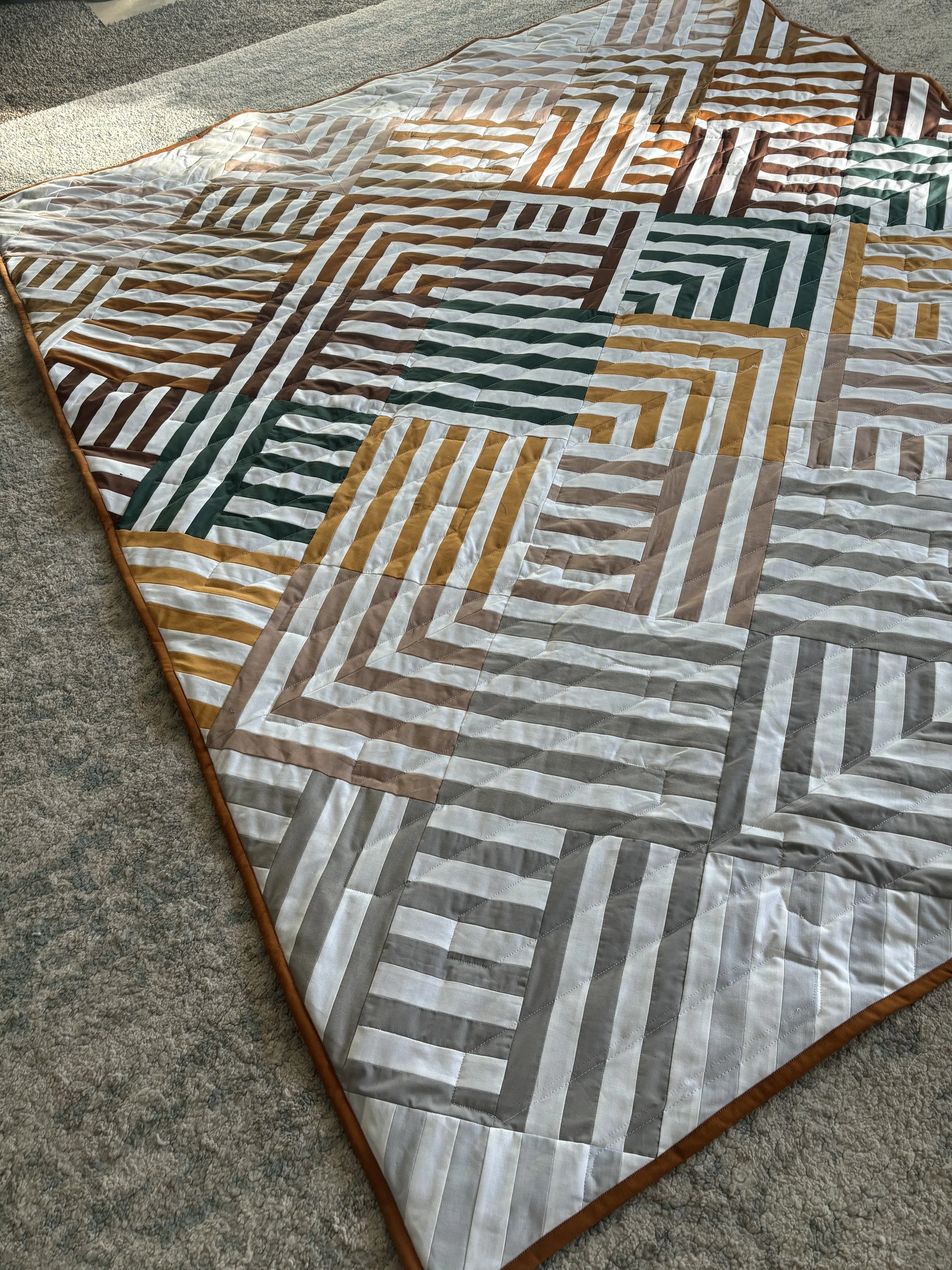 A patchwork quilt with various geometric designs and floral patterns in shades of beige, cream, and teal, with a small part of a baby in the bottom right corner.