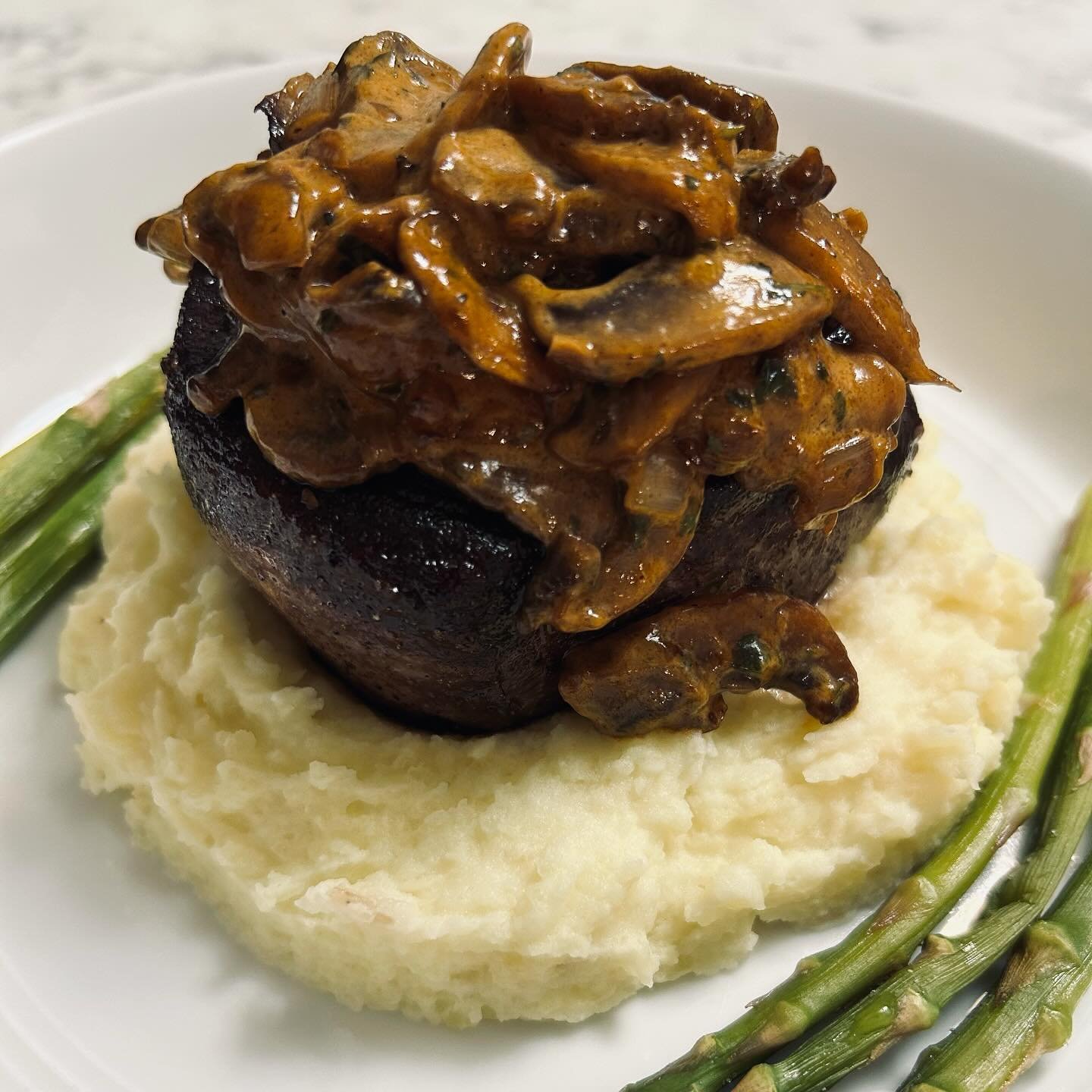 Beef steak topped with mushroom gravy served over mashed potatoes with asparagus on the side.