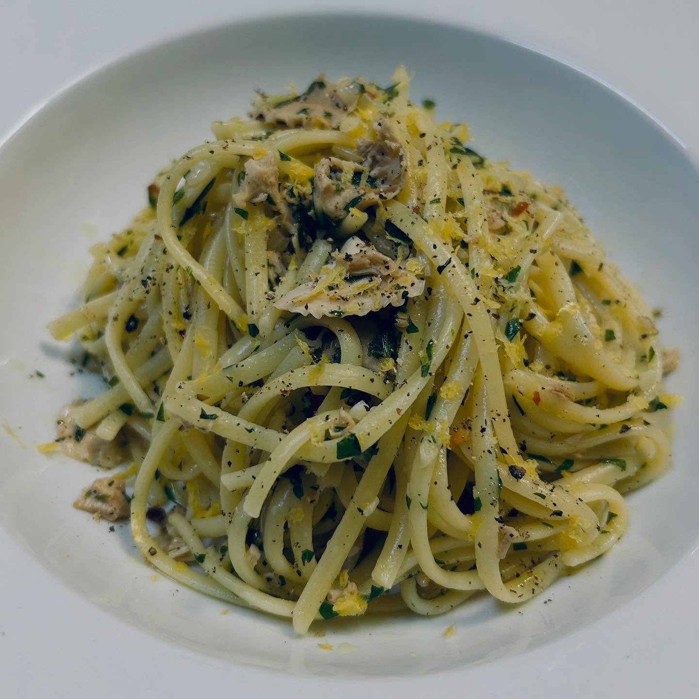A plate of spaghetti pasta mixed with herbs, black pepper, and small pieces of chicken or seafood.